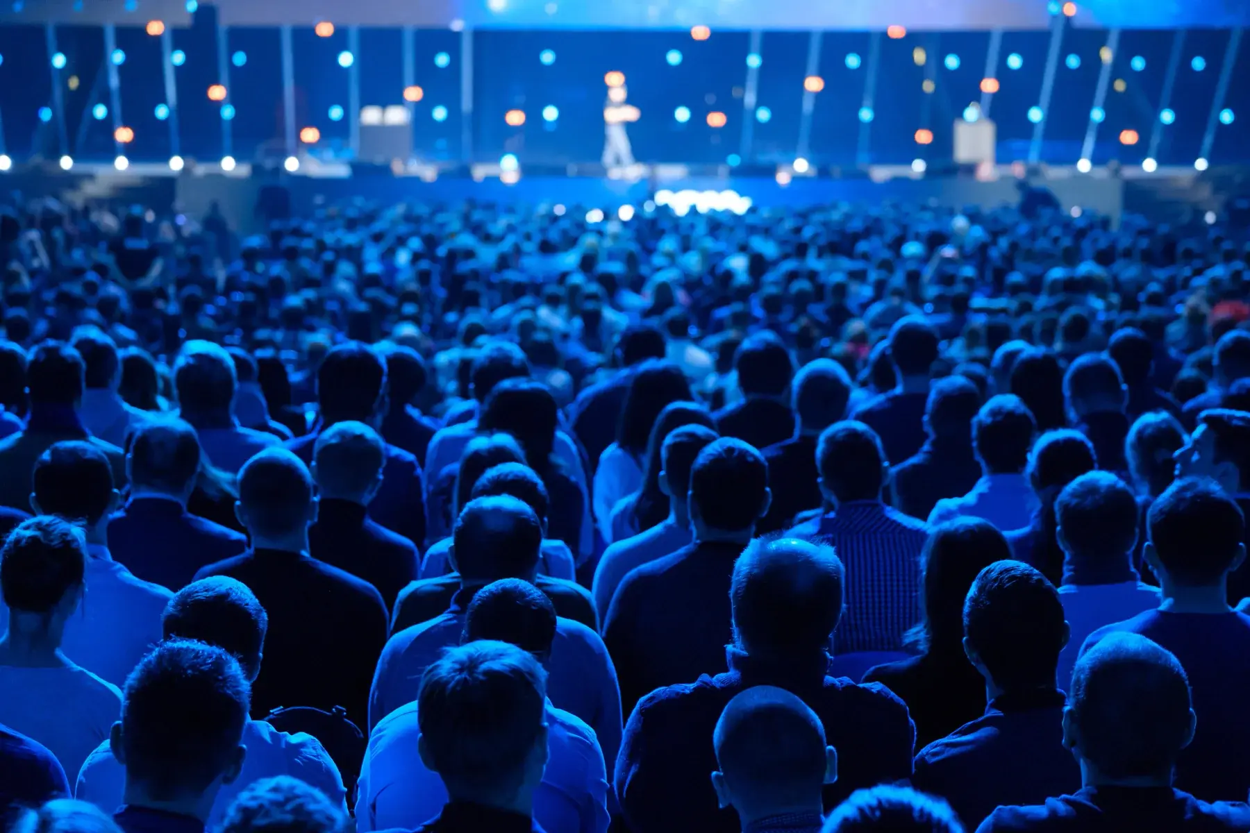 Packed general session audience facing a brightly lit stage in blue light