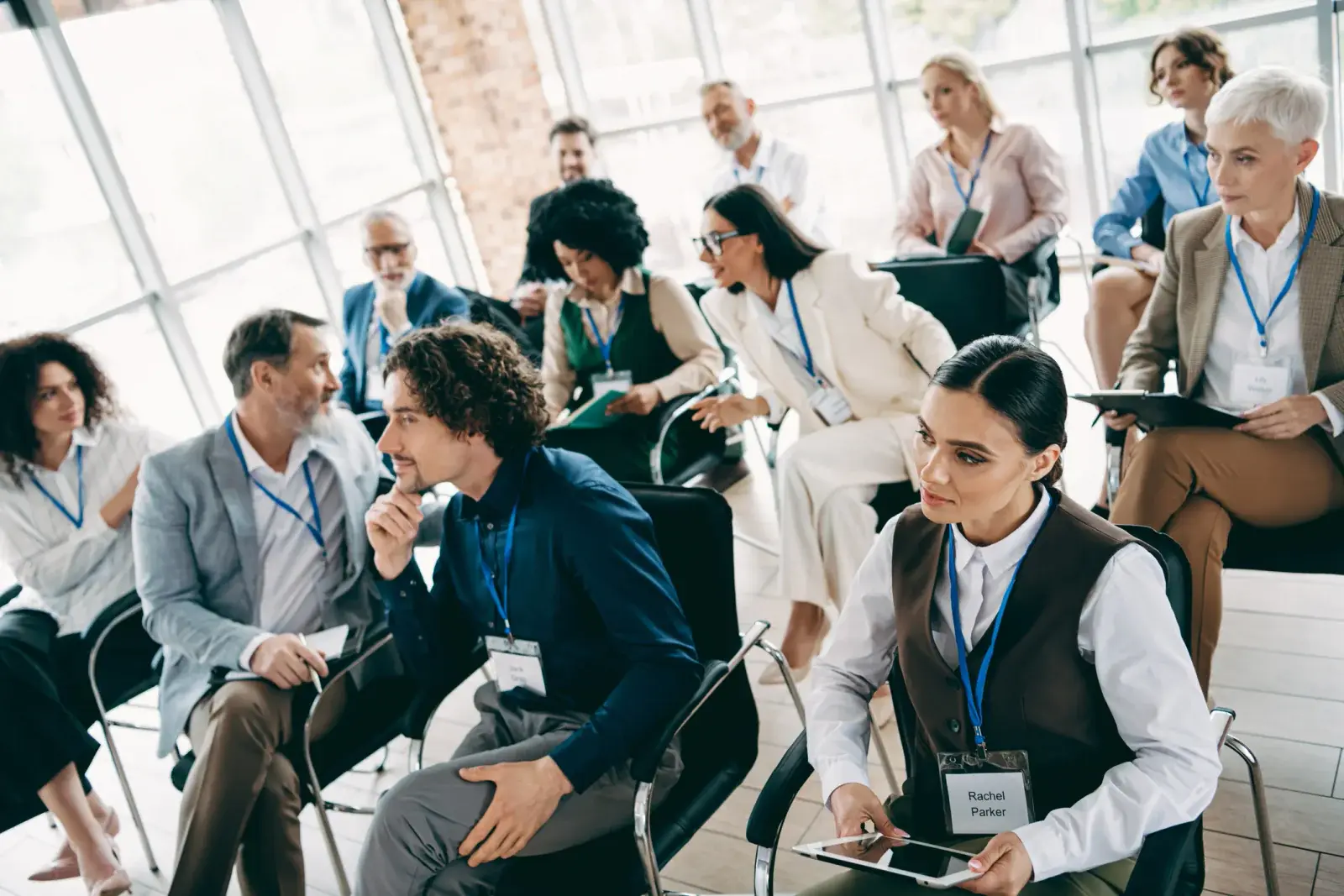 Attendees wearing name badges seated in a breakout session, one holding a tablet