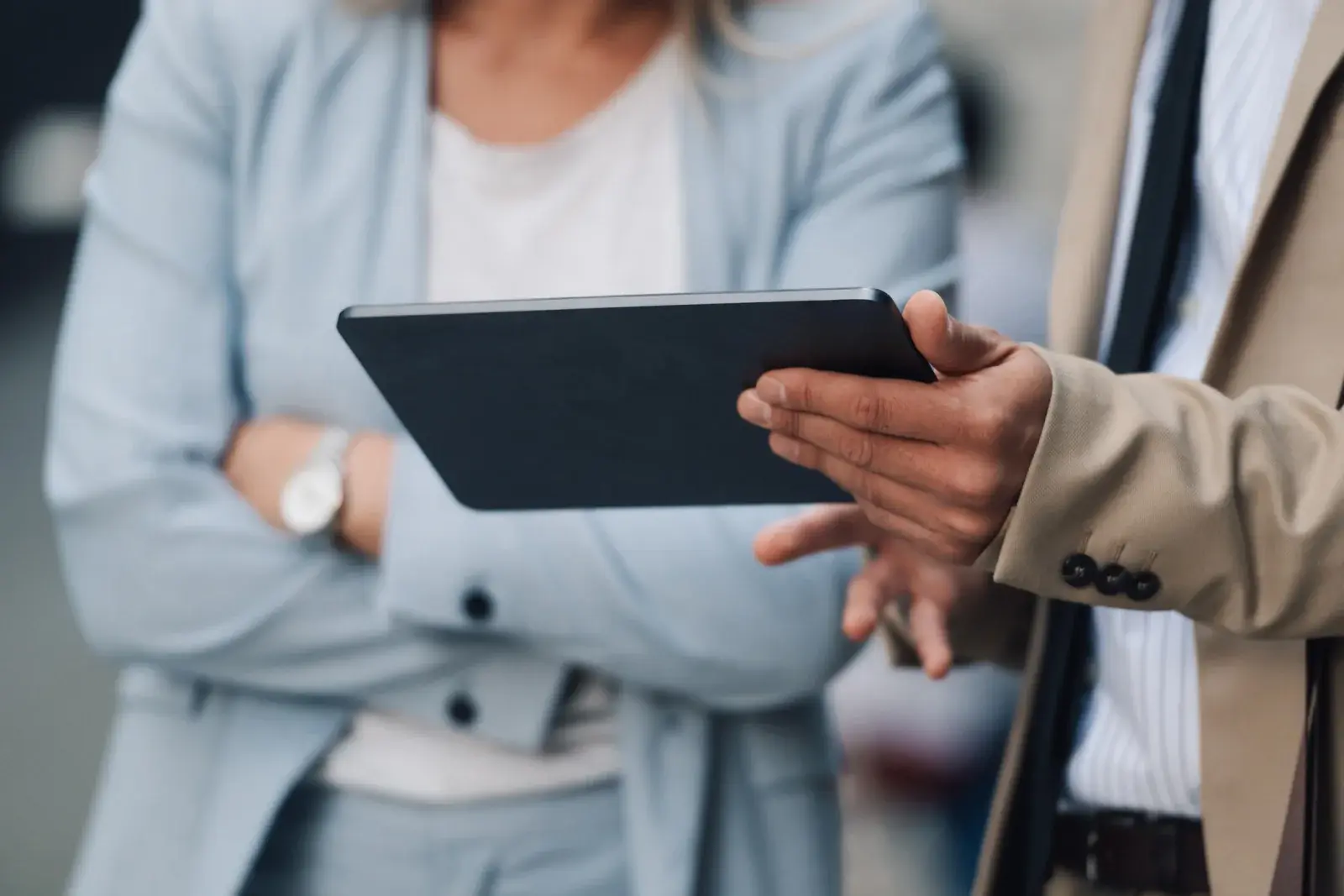 Close-up of a person holding a tablet while talking with a colleague