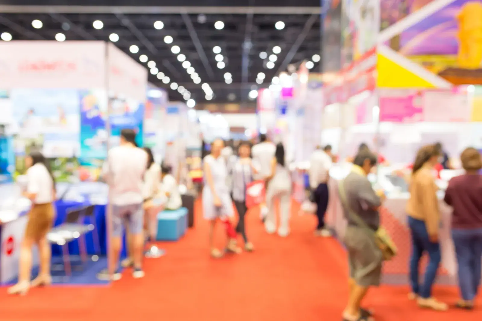 Blurred view of attendees walking a red-carpeted aisle between exhibit booths