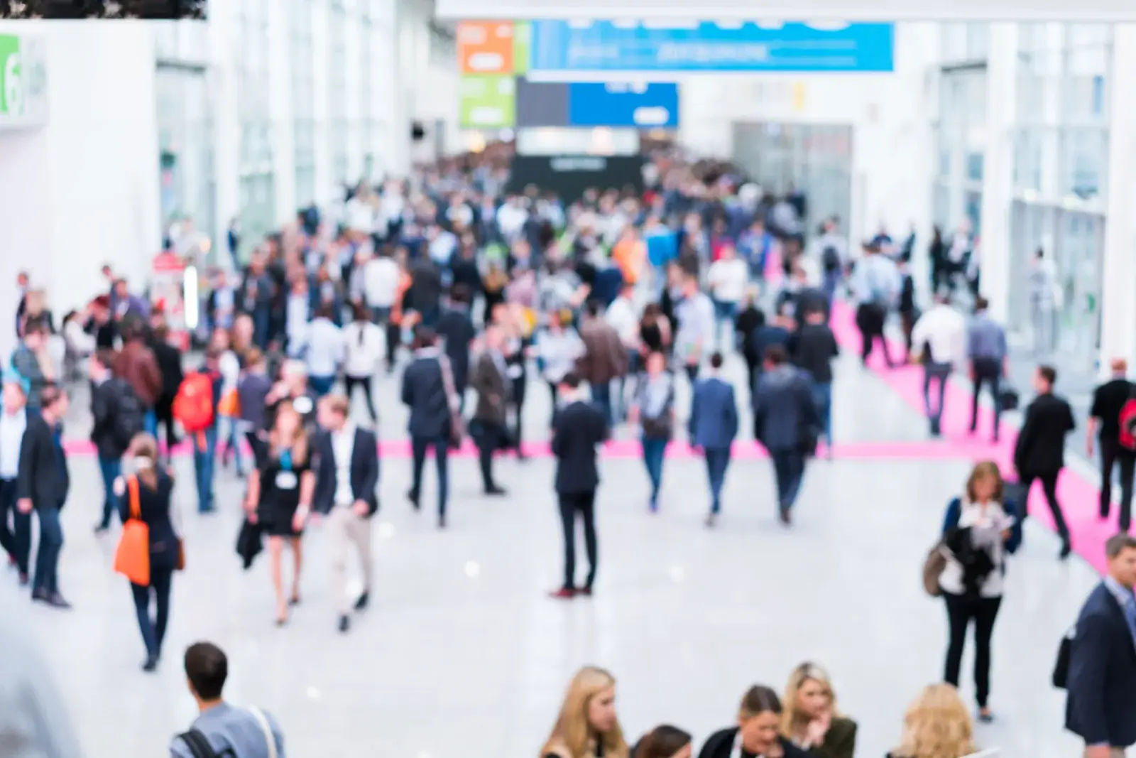 Crowd of attendees walking through a bright convention center concourse, seen from above and out of focus