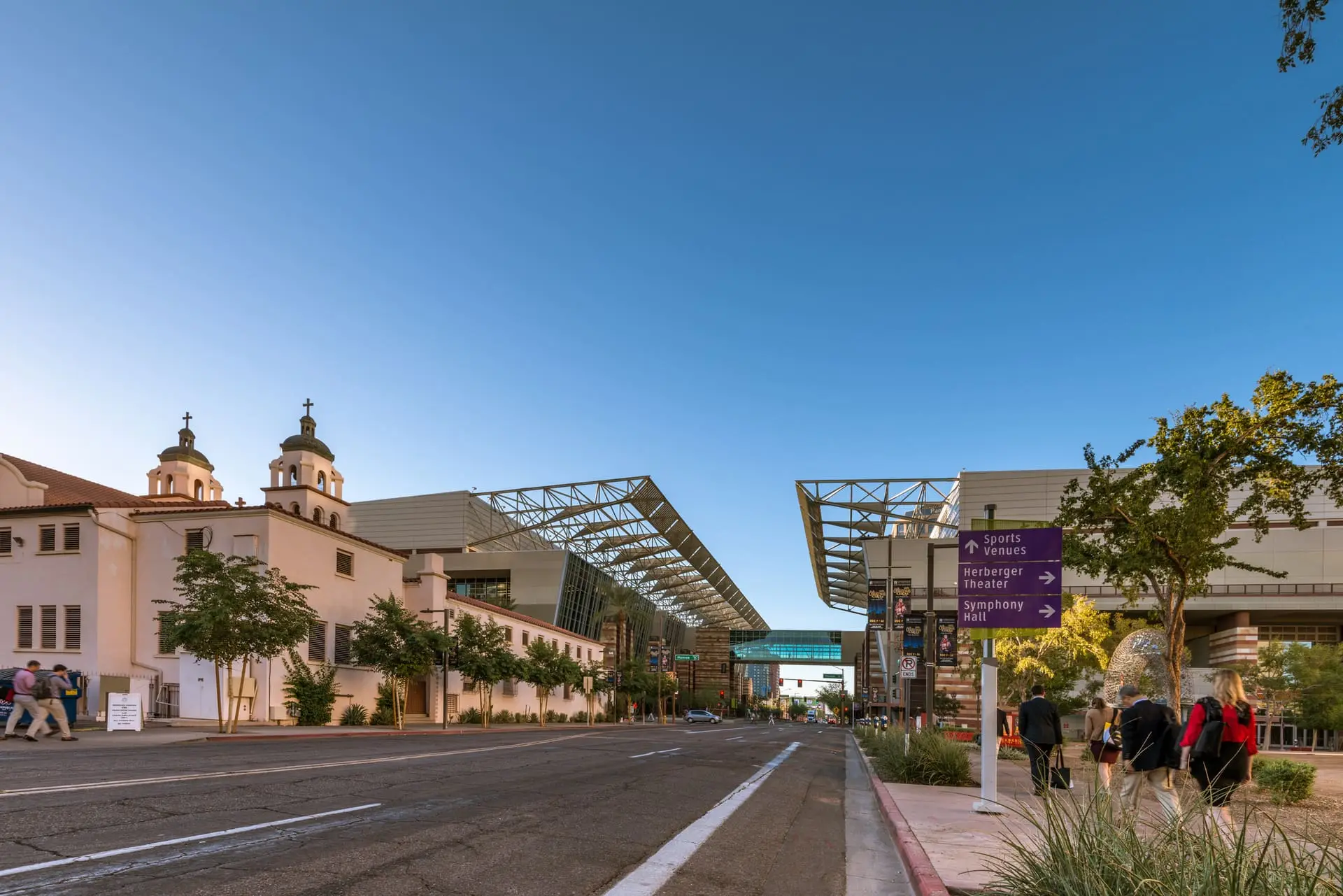 Phoenix Convention Center's steel canopies along a downtown street beside a historic mission-style church, with attendees walking on the sidewalk